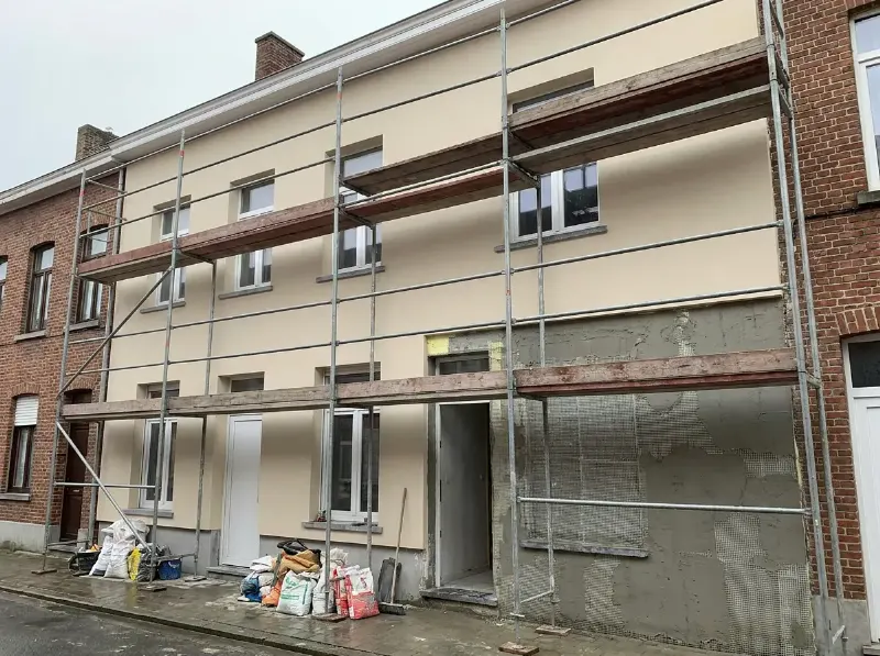 Gevel van een rijwoning met een verse laag buitenpleister op isolatieplaten, steiger nog opgesteld